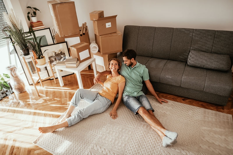 Couple sitting in new home with moving boxes around them.