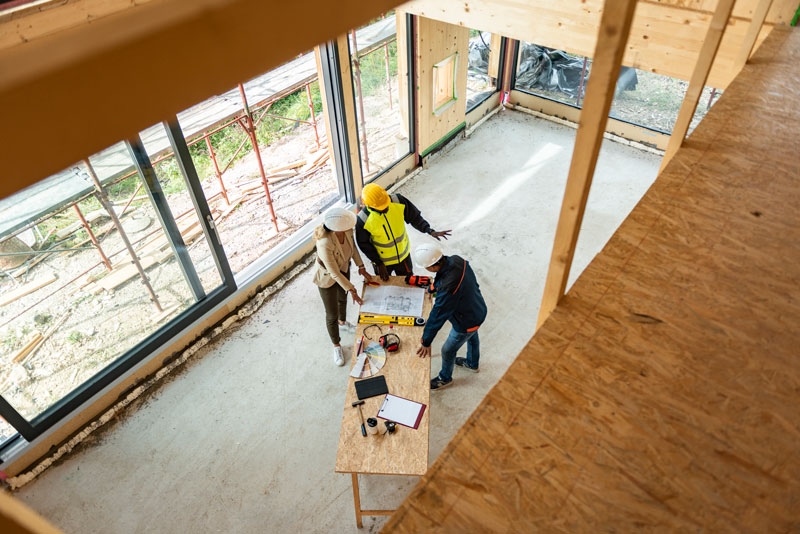 Workers in a partially built house looking at plans on a table