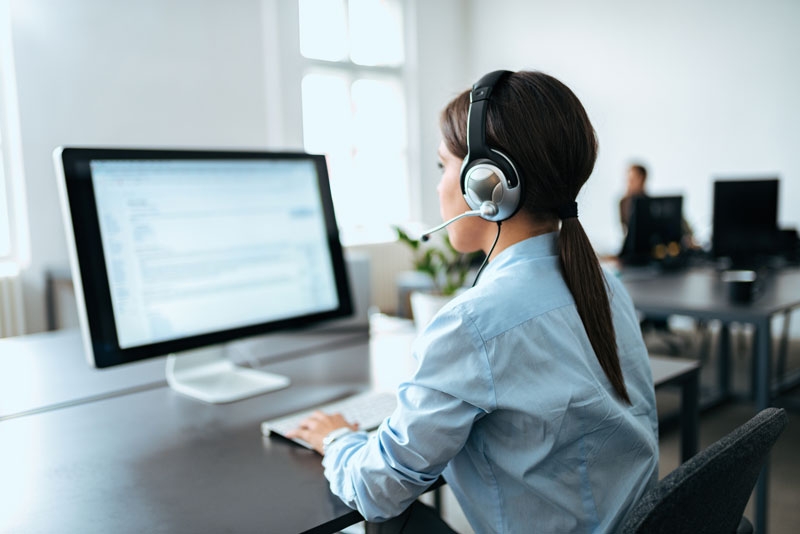 A worker sits at a computer wearing a headset