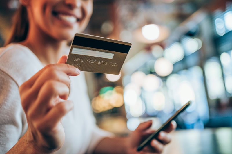 A woman smiles as she holds a credit card in one hand and a cell phone in the other hand