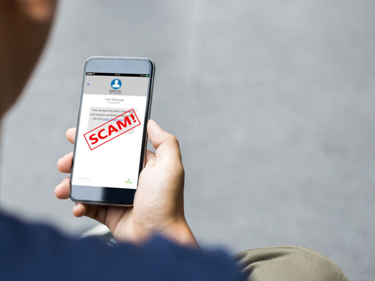 A man is holding a smart phone that says Scam on the screen in big red letters.